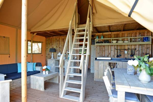 Vista interna di una tenda da campeggio al Papillon Country Resort con mobili in legno, una scala e zona cucina.