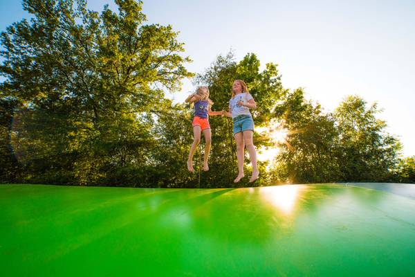 Due ragazze saltano su un trampolino con alberi sullo sfondo.