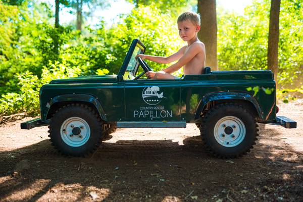 Un bambino piccolo guida un'auto giocattolo verde in un bosco.
