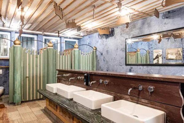 Interno di una sala doccia moderna con tre lavandini bianchi e divisori verdi al Caravan Park Sexten.
