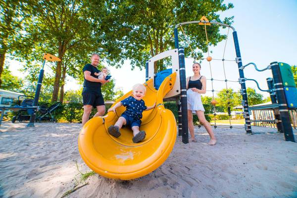 Bambini che giocano su un parco giochi in un campeggio con padre, bambino e madre.