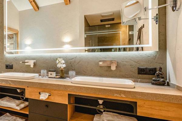 Bathroom in Erlebnis Resort Aufenfeld with two sinks, mirrors, and wooden shelves.