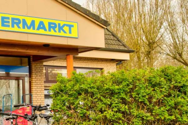 Vorderseite des Wulfener Hals Supermarkts mit gelbem Schild und geparkten Fahrrädern davor