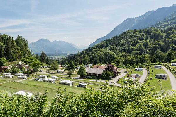 Vista aérea del camping Alpencamping Nenzing con autocaravanas y casas móviles entre árboles y montañas