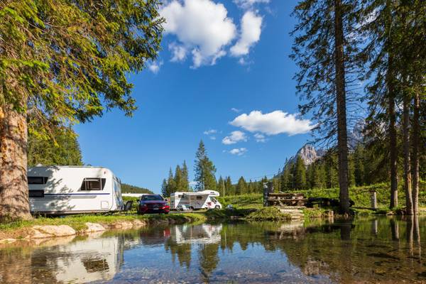 Campeggio Caravan Park Sexten con roulotte, auto e uno stagno sotto un cielo blu.
