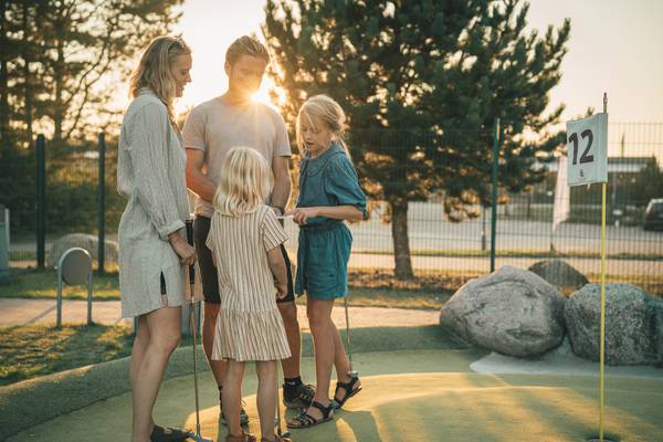 Una familia juega al mini golf en el Feddet Strand Resort con un brillante atardecer en el fondo.