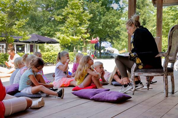 Kinderen luisteren naar een vrouw die op een campingterras leest