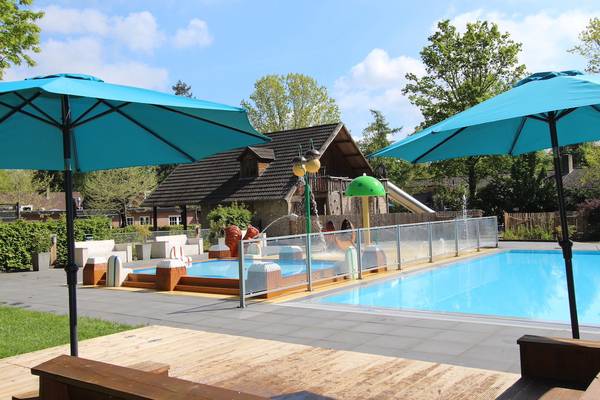 Zwembadgebied bij Camping De Wildhoeve met blauwe parasols en een waterglijbaan.