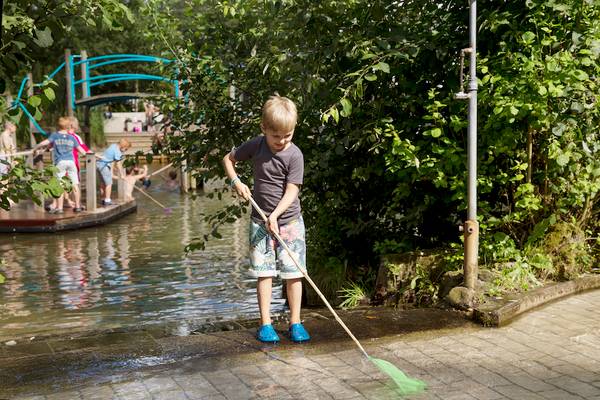 Een jongen maakt het terrein schoon met een net bij een vijver in Camping De Wildhoeve.