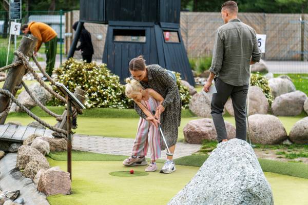 Una familia en el campo de mini golf de Feddet Strand Resort con rocas y una estructura negra al fondo.