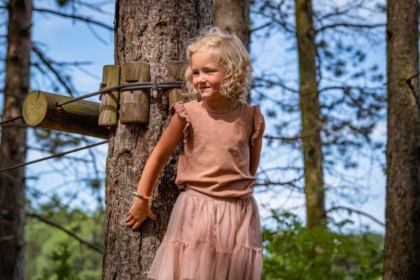 Niña pequeña parada en un árbol en el camping Feddet Strand Resort