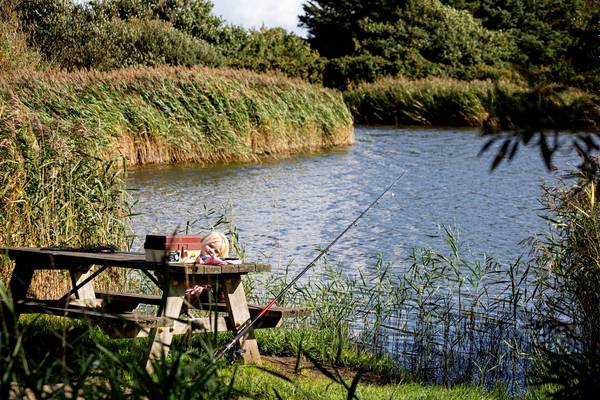 Ein Mädchen angelt an einem Picknicktisch am See im Hvidbjerg Strand Feriepark