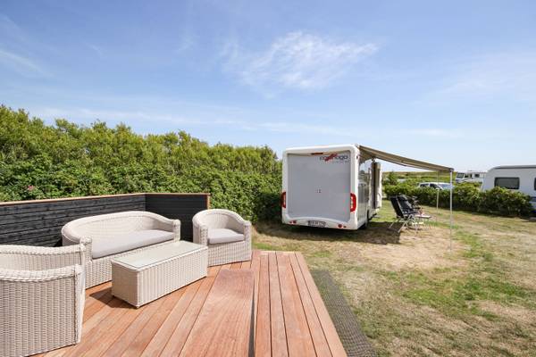 Ein Wohnwagen mit Vorzelt auf einer Holzterrasse mit Korbmöbeln im Hvidbjerg Strand Feriepark.