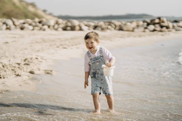 Ein Junge steht im Wasser am Strand mit einer Eimer in der Hand.