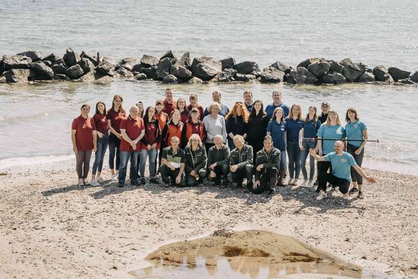 Teamfoto der Campingplatz-Mitarbeiter am Strand mit Felsen und Wasser im Hintergrund.