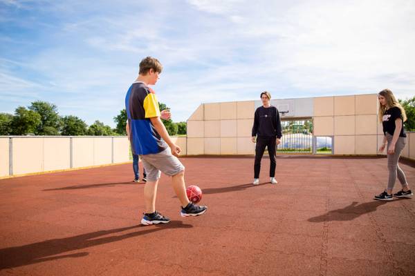 Jugendliche spielen Fußball auf einem Campingplatz mit einem Basketballkorb im Hintergrund.