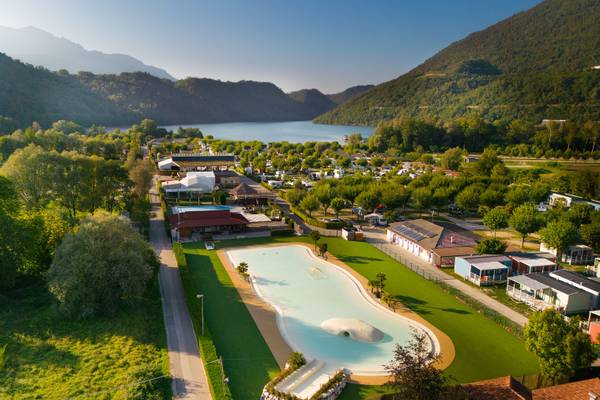 Luftfoto af Lago Levico Camping Village med en sø og bjerge i baggrunden.