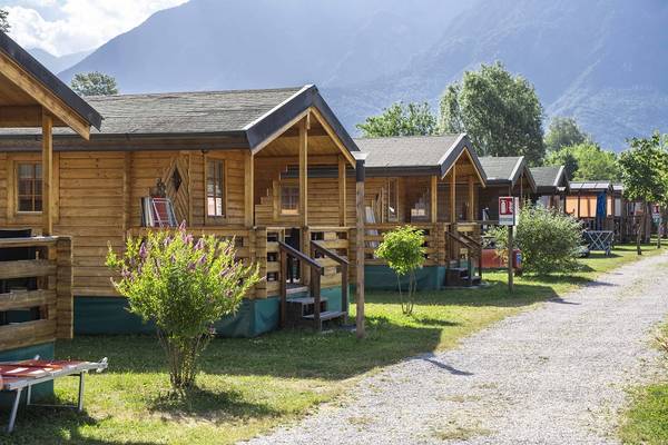 En række træhytter i Lago Levico Camping Village med bjerge i baggrunden.