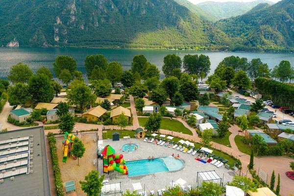 Vue aérienne du bungalow glamping Lago Idro avec piscine, aire de jeux et paysage montagneux.