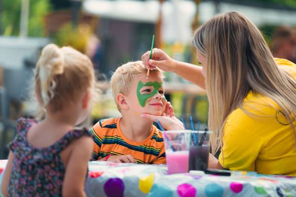 Une femme applique de la peinture verte sur le visage d'un garçon, une jeune fille regarde.