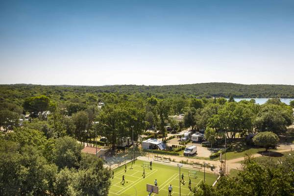 Terrain de sport au camping Vestar avec plusieurs personnes jouant, des camping-cars et des arbres.
