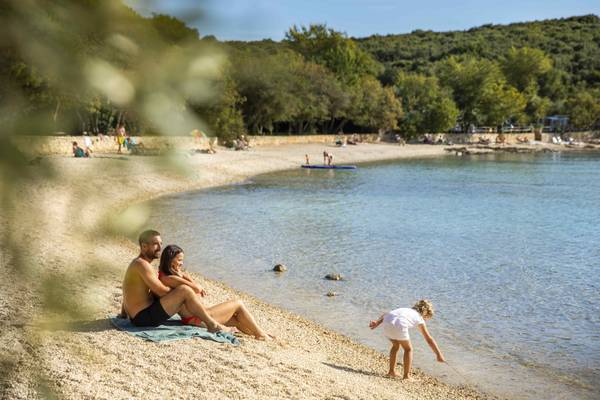 Une famille sur la plage du Camping Vestar, avec une femme et un enfant près de l'eau.