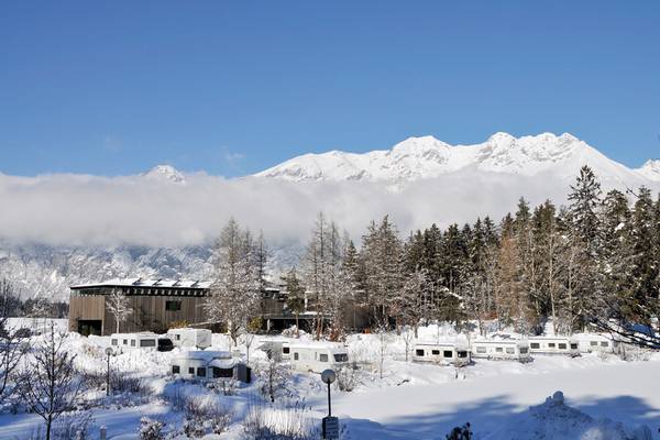 Winteransicht des Ferienparadies Natterer See Campingplatzes mit verschneiten Bergen und Wohnwagen.