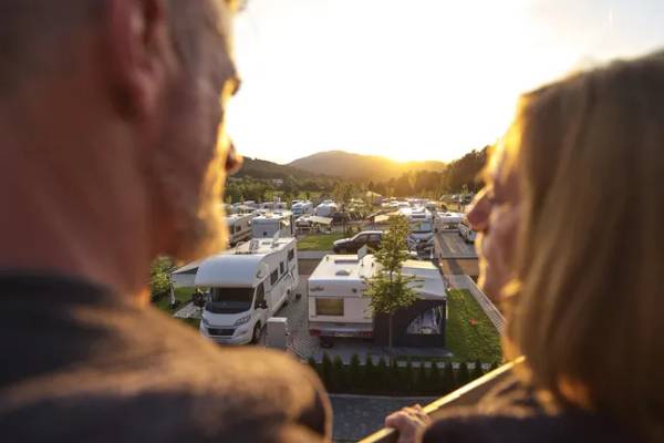Udsigt fra en balkon på Camping Resort Bodenmais med campingvogne og en solnedgang i baggrunden.