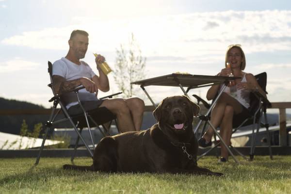 Et par med hund, der nyder et måltid på terrassen på en campingplads.