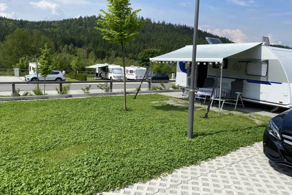 Campingvogn parkeret på en campingplads med træer og bjerge i baggrunden