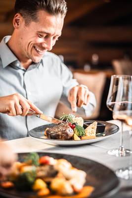 Un hombre come un filete con verduras y copas de vino sobre la mesa en un restaurante.