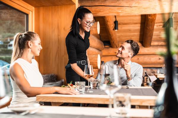Comida en el restaurante del camping de los Alpes Nenzing con un camarero sonriente e invitados