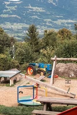 Zona de juegos en el camping de los Alpes Nenzing con un tractor agrícola en el fondo.