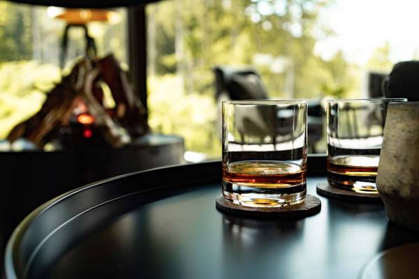 Dos vasos de whisky sobre una mesa frente a una chimenea.