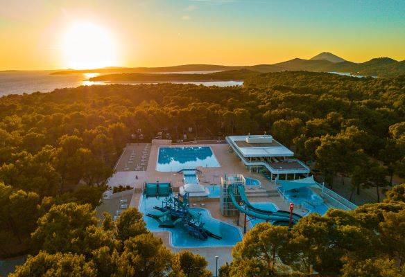 Vista aérea del parque acuático del Camping Cikat con piscinas y toboganes al atardecer.