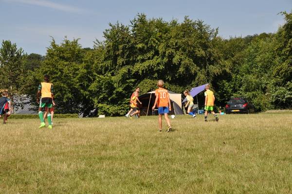 Kinderen voetballen op de camping met bomen en tenten op de achtergrond.