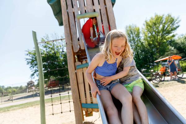 To børn glider ned ad en rutsjebane i en legeplads på Vakantiepark De Twee Bruggen.