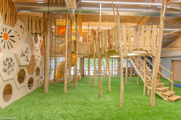 Innenspielplatz des Camping Wirthshof mit Holzkonstruktionen, Rutschen und grünem Teppich.