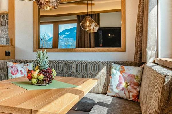 Interior of Erlebnis Resort Aufenfeld showing a cozy living area with a wooden table, a bowl of fruit, and a kitchen in the background.