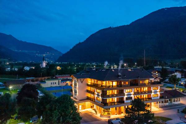 Evening view of Erlebnis Resort Aufenfeld with mountains and illuminated buildings.