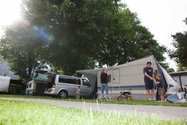 Family setting up a tent at Erlebnis Resort Aufenfeld campsite with trees and a van in the background.