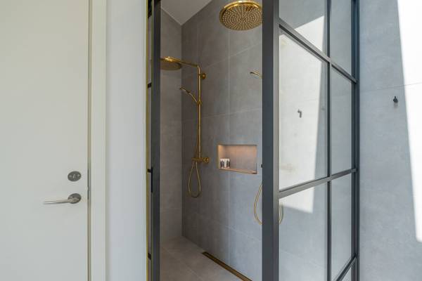 Área de ducha en Feddet Strand Resort con azulejos grises y accesorios dorados.