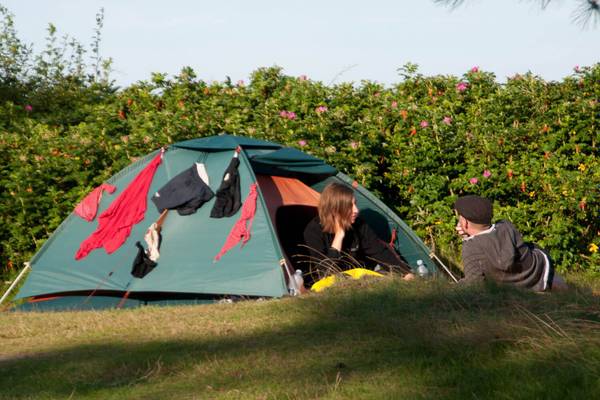 Dos personas sentadas fuera de una carpa verde en un camping.