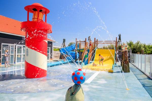 Freizeitpark mit Leuchtturm und Wasserspiel an einem sonnigen Tag.