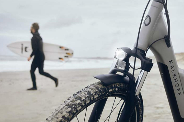 Bicicleta KalkhoFf en la playa de Jambo Feriepark con un surfista en el fondo