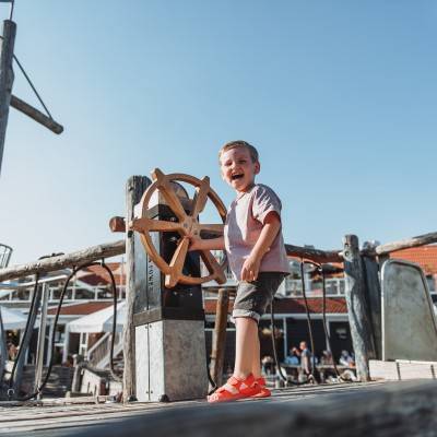 Junge lacht am Steuerrad des Campingplatzes Strandpark De Zeeuwse Kust.