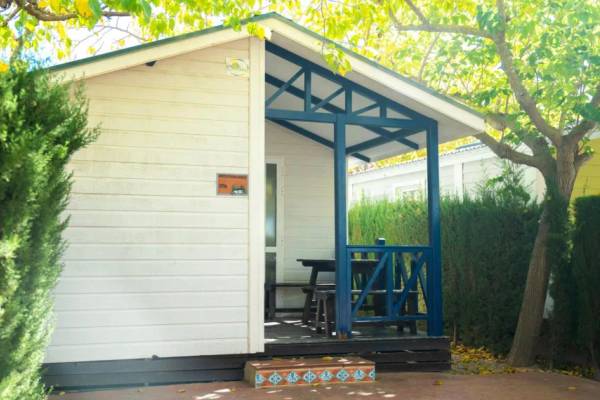 Une résidence de camping blanche avec une véranda bleue et une table sous un arbre.
