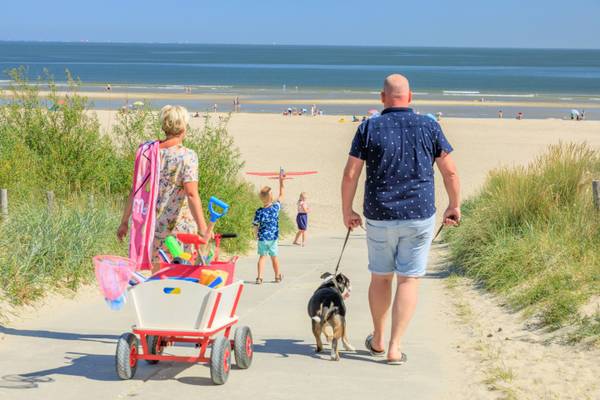 Eine Familie mit Hund geht am Strand spazieren mit einem Wagen voller Spielzeug