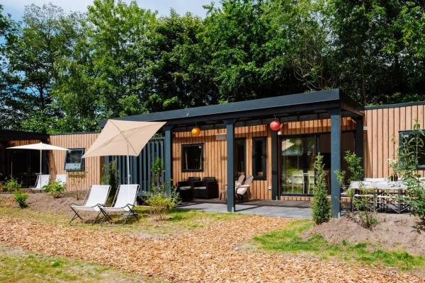 Un chalet moderno nel campeggio Papillon Country Resort con mobili da esterno e alberi sullo sfondo.