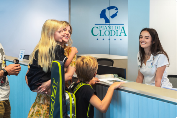 En familie med to børn og en mand ved receptionen på Piani di Clodia campingplads.